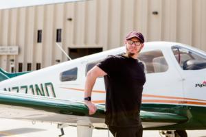 Josh leans against the wing of an airplane.