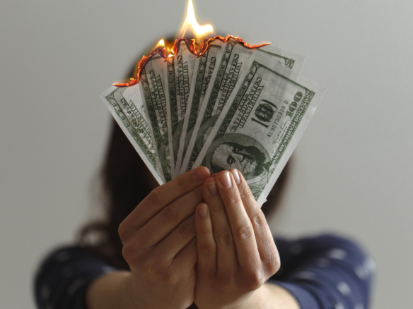 A girl holds several $100 bills that are on fire.