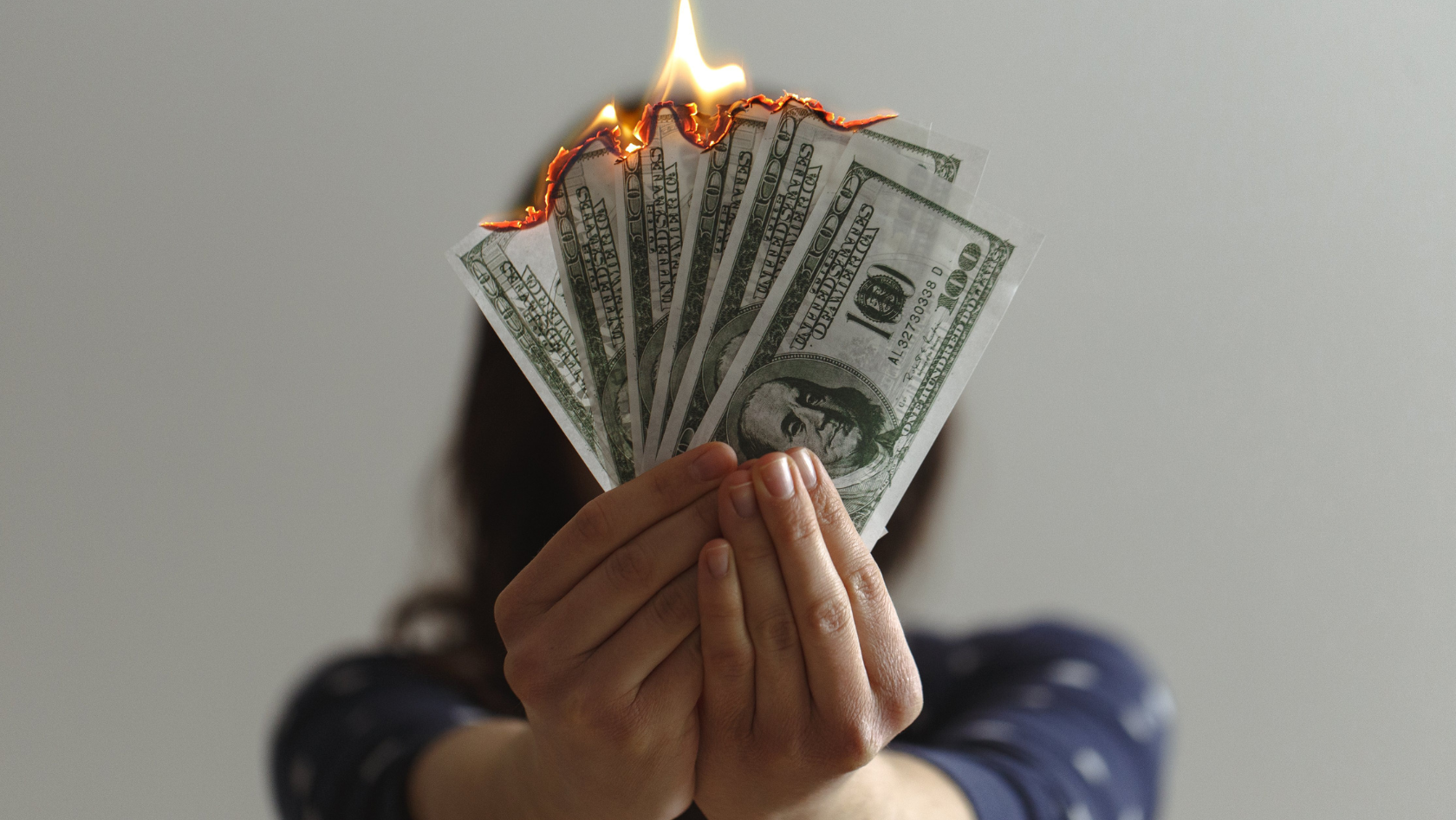 A girl holds several $100 bills that are on fire.