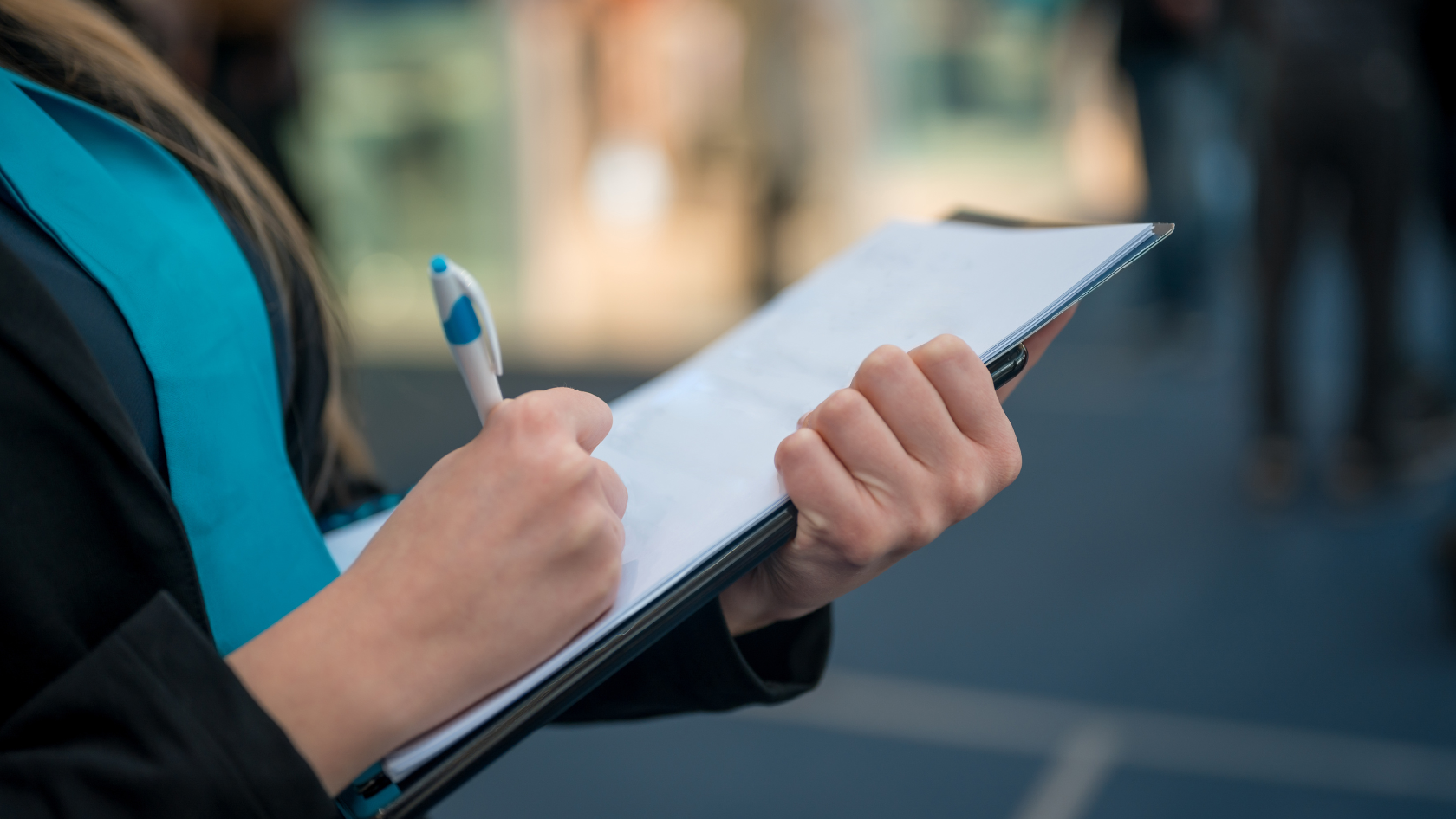 Close-up of a woman writing on a clipboard with a pen during a business event or conference.