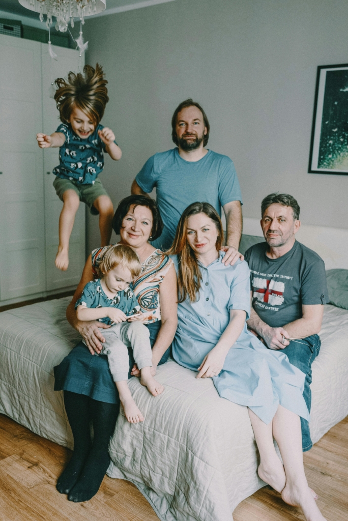 Mulitgenerational family sits on a master bedroom bed while one of the children jumps